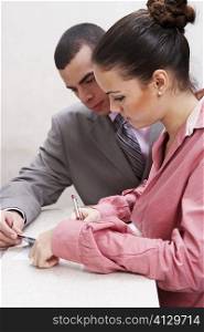 Side profile of a businesswoman writing with a businessman holding a credit card beside her