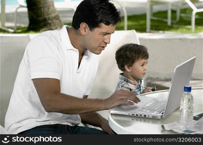 Side profile of a father working on a laptop with his son sitting beside him