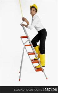 Side profile of a female architect climbing a ladder and holding a tape measure