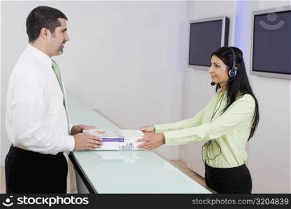 Side profile of a female customer service representative giving books to a businessman