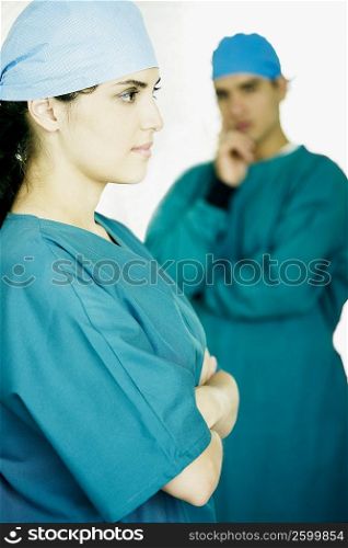 Side profile of a female doctor standing with her arms crossed and a male doctor standing in the background
