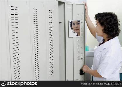 Side profile of a female looking at a mirror on the door of a locker
