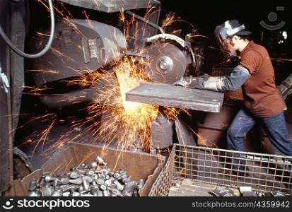 Side profile of a foundry worker working on a metal saw in a factory, Wisconsin, USA