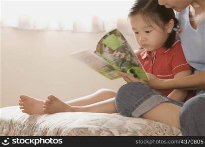 Side profile of a girl and her mother reading a book