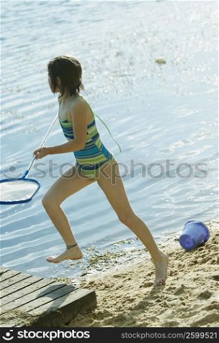 Side profile of a girl holding a fishing net and running at the lakeside