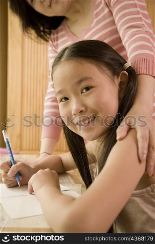 Side profile of a girl holding a pen with her mother standing beside her