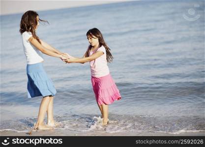 Side profile of a girl holding hands of her sister on the beach