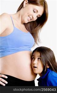 Side profile of a girl listening to a pregnant young woman&acute;s abdomen