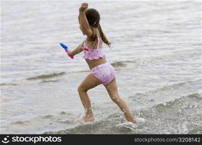 Side profile of a girl running on the beach and holding a sand pail