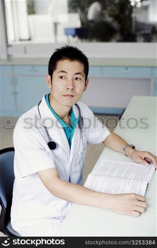 Side profile of a male doctor sitting at the table and holding a book