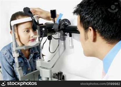 Side profile of a male optometrist examining a girl&acute;s eye