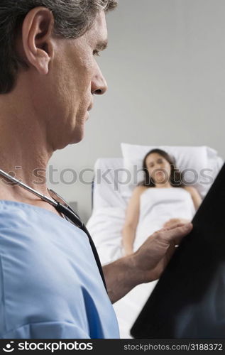 Side profile of a male surgeon examining an X-Ray report with a patient in the background