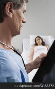 Side profile of a male surgeon examining an X-Ray report with a patient in the background