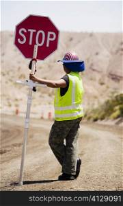 Side profile of a man holding a stop sign on a dirt road