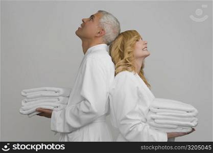Side profile of a mature couple standing back to back and holding folded towels