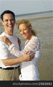 Side profile of a mature couple standing on the beach and smiling