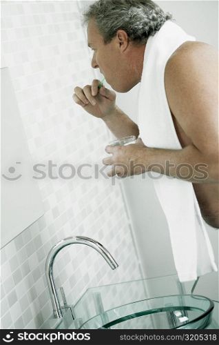 Side profile of a mature man brushing his teeth in a mirror
