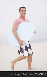 Side profile of a mature man carrying a body board on the beach