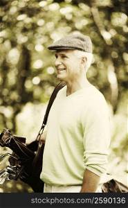 Side profile of a mature man carrying a golf bag and smiling