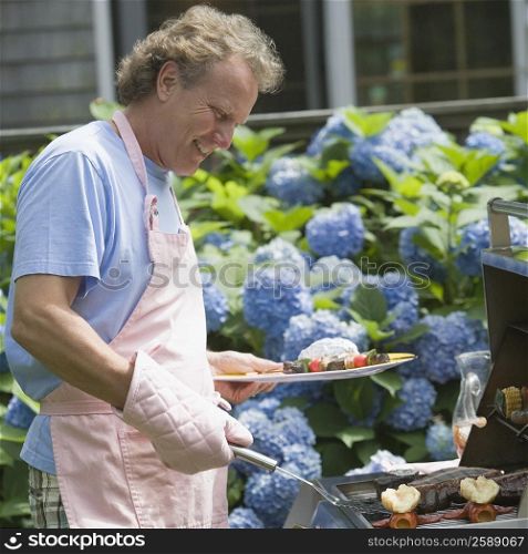 Side profile of a mature man cooking food on a barbecue grill