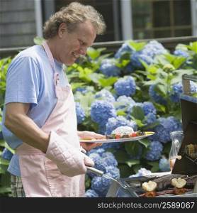 Side profile of a mature man cooking food on a barbecue grill