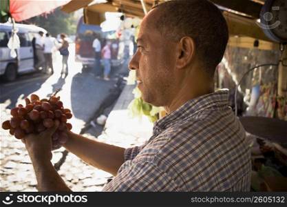 Side profile of a mature man holding a bunch of red grapes, Santo Domingo, Dominican Republic