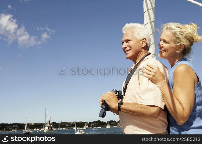 Side profile of a mature man holding a pair of binoculars with a mature woman standing behind him