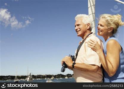 Side profile of a mature man holding a pair of binoculars with a mature woman standing behind him