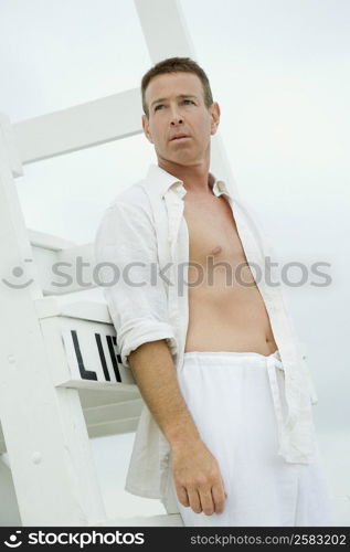 Side profile of a mature man leaning against a lifeguard hut