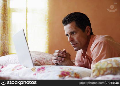 Side profile of a mature man lying on the bed and looking at a laptop