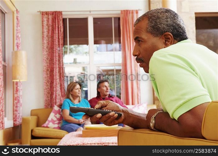 Side profile of a mature man operating a remote control with a mature couple sitting beside him