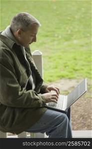 Side profile of a mature man sitting in a lawn and using a laptop