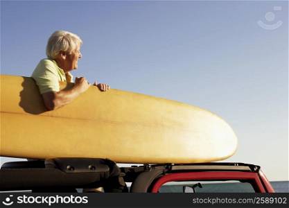 Side profile of a mature man sitting in a sports utility vehicle and holding a surfboard
