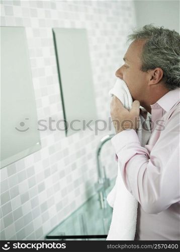Side profile of a mature man wiping his face with a towel in front of a mirror