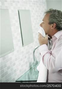 Side profile of a mature man wiping his face with a towel in front of a mirror