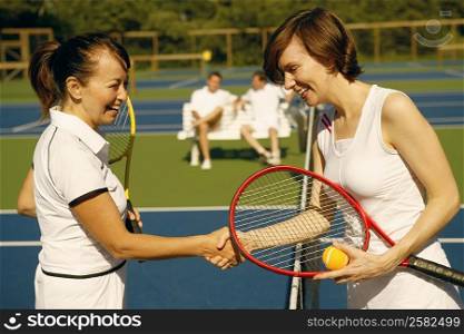 Side profile of a mature woman and a mid adult woman shaking hands on a tennis court