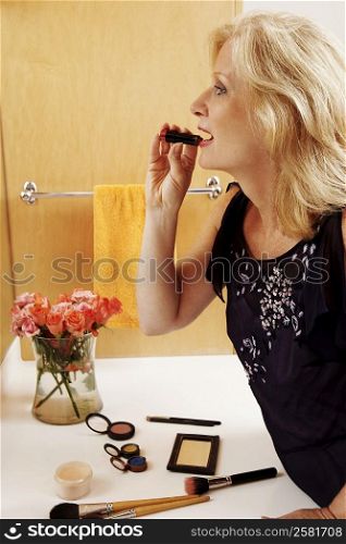 Side profile of a mature woman applying lipstick in the bathroom