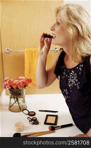 Side profile of a mature woman applying lipstick in the bathroom