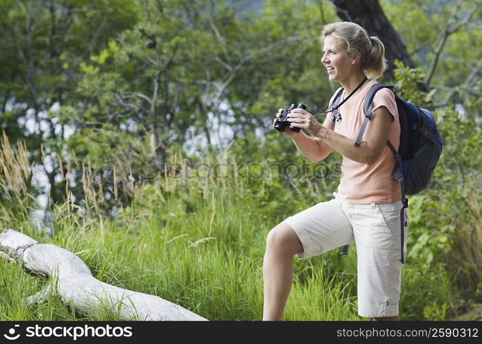 Side profile of a mature woman holding binoculars in a forest