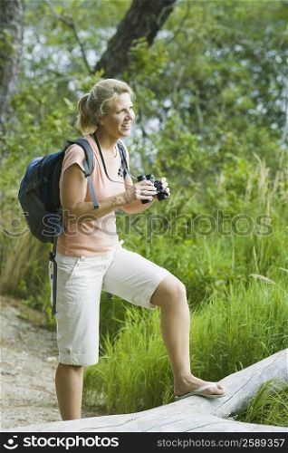 Side profile of a mature woman holding binoculars in a forest and smiling