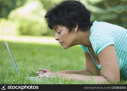 Side profile of a mature woman lying on grass and using a laptop