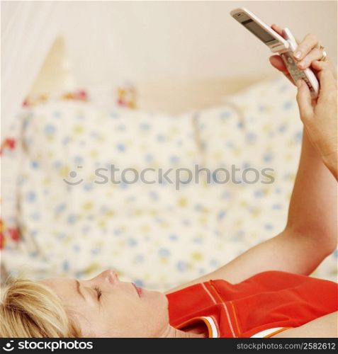 Side profile of a mature woman lying on the bed and holding a flip phone
