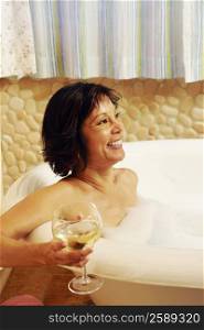Side profile of a mature woman sitting in a bathtub and holding a glass of wine