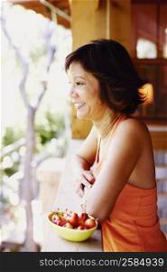 Side profile of a mature woman standing in a balcony with a bowl of cherries beside her
