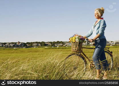 Side profile of a mature woman standing in a field with a bicycle