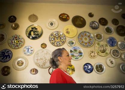 Side profile of a mature woman standing in front of a wall decorated with ceramics