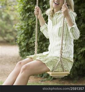 Side profile of a mature woman swinging on a rope swing and smiling