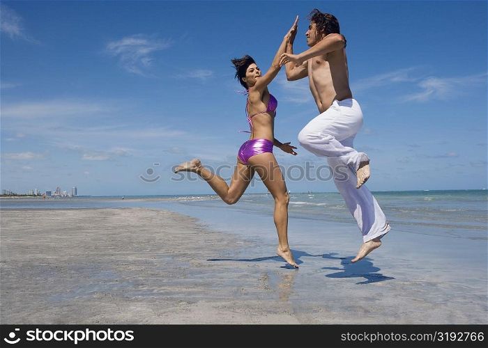 Side profile of a mid adult couple doing high-five on the beach