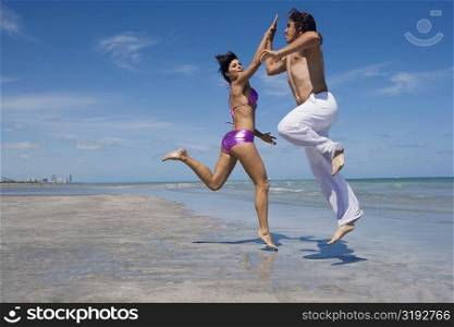 Side profile of a mid adult couple doing high-five on the beach