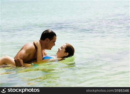 Side profile of a mid adult man and a young woman embracing each other in the sea